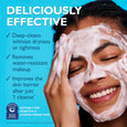 Person applying white whipped cream cleanser to face against blue background.