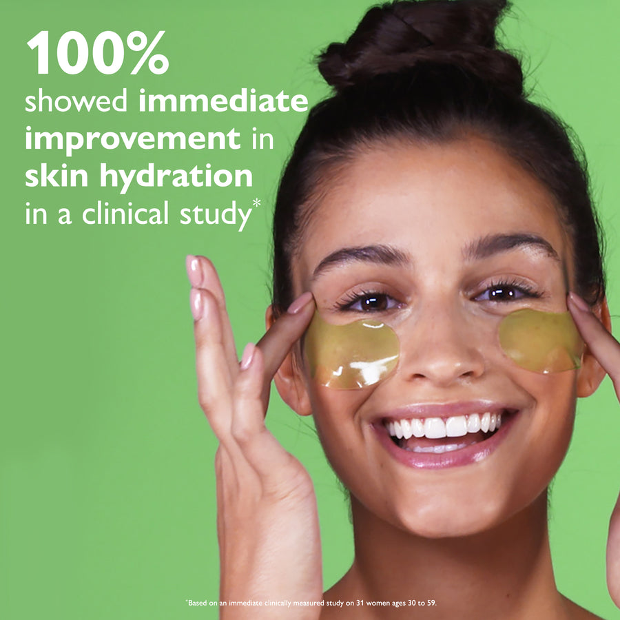 Woman wearing golden gel eye patches under eyes against green background.