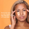 Person applying white gel eye patches under eyes against orange background.