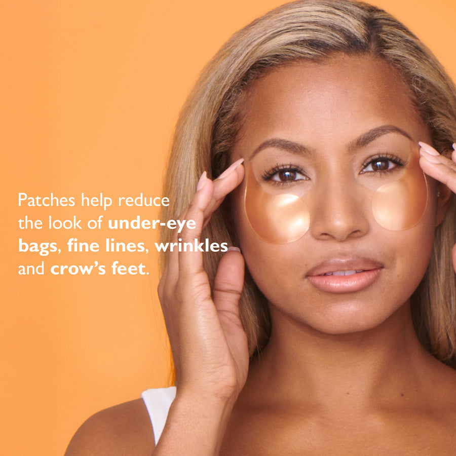 Person applying white gel eye patches under eyes against orange background.