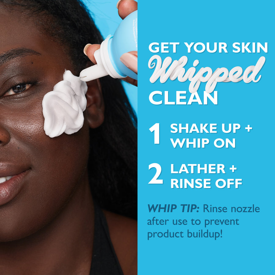 Person applying white whipped cleanser to face from pump bottle against blue background.