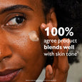 Person with deep skin tone applying beige-toned liquid primer to cheek, demonstrating product blending and finish.