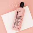 Pink strawberry scrub with visible red particles in a 250 ml bottle with black cap, displayed with product swatches on pink b