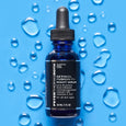 Dark blue glass dropper bottle labeled "Retinol Fusion PM Night Serum" on blue background surrounded by water droplets.