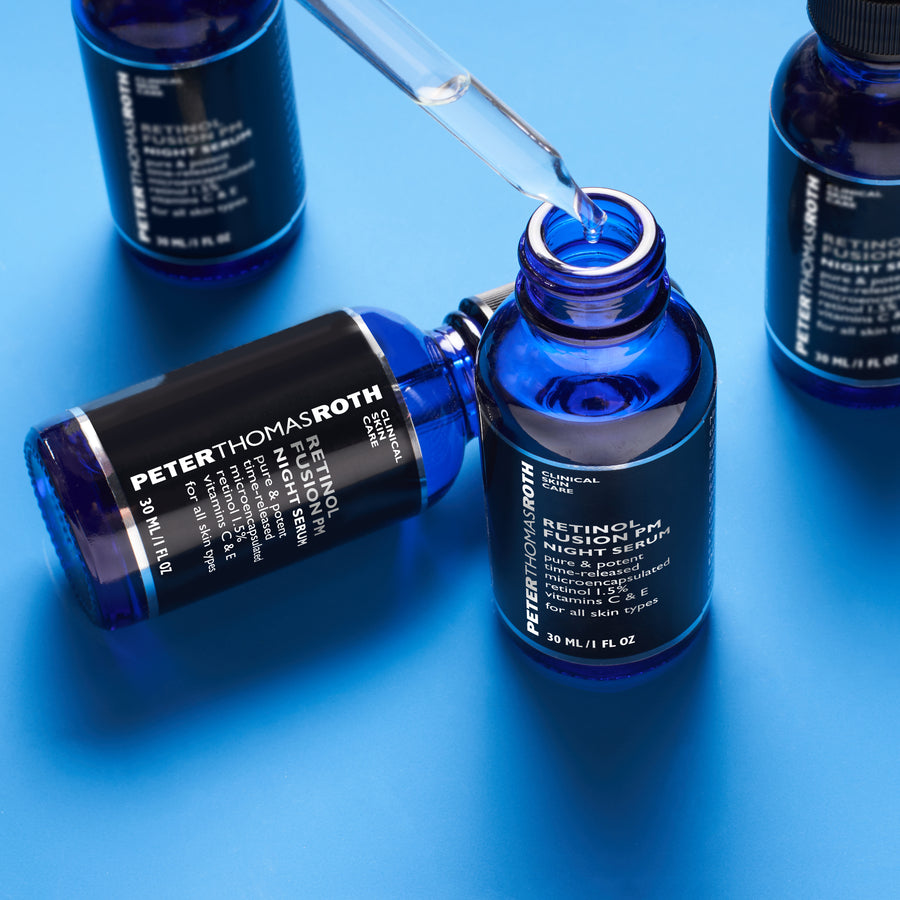 Blue glass bottles of Retinol Fusion PM Night Serum with dropper applicator on blue background.