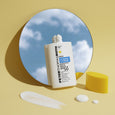 White bottle of Max Vitamin D-Fense sunscreen serum SPF 50 displayed with product swatches and yellow geometric shapes agains