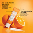 Orange tube of Potent-C Niacinamide Discoloration Treatment surrounded by fresh orange halves on yellow background.