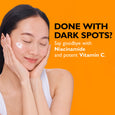 Woman with dark hair applying white cream to cheekbone against orange background.