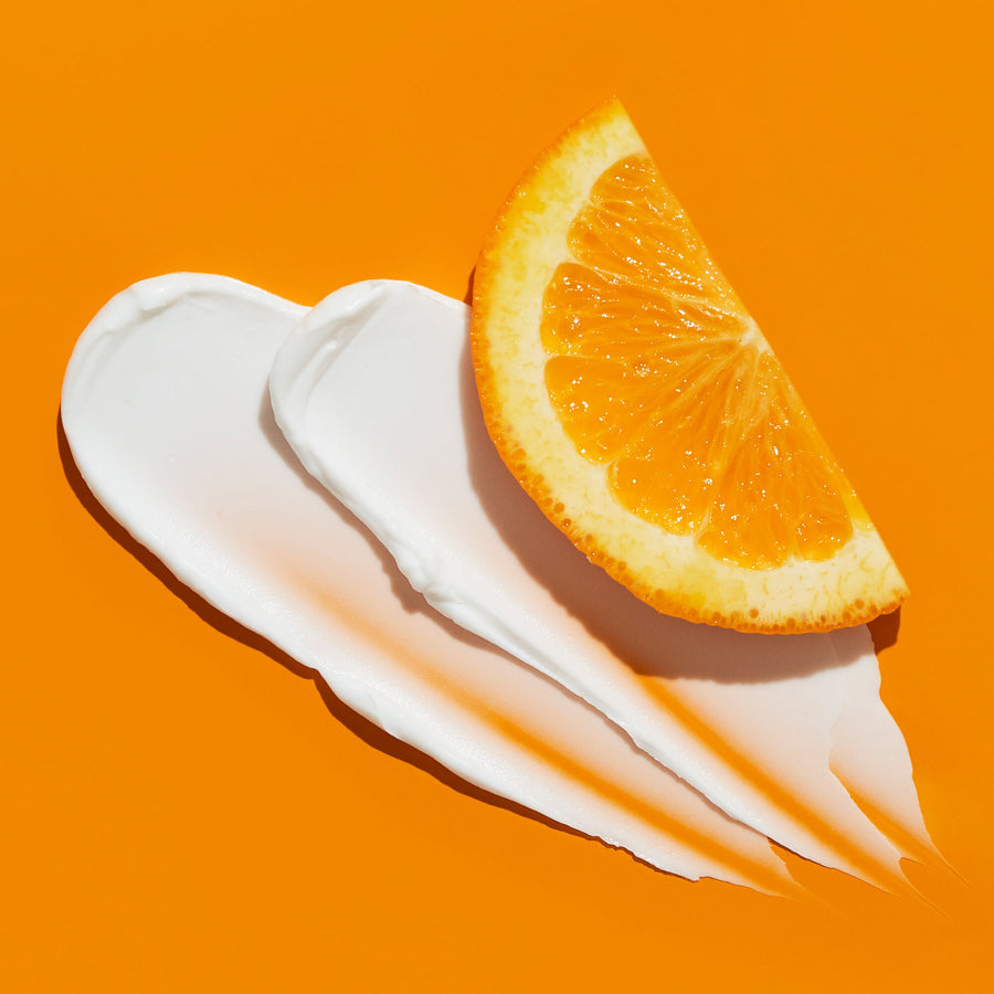White cream swatches with an orange citrus slice on an orange background.