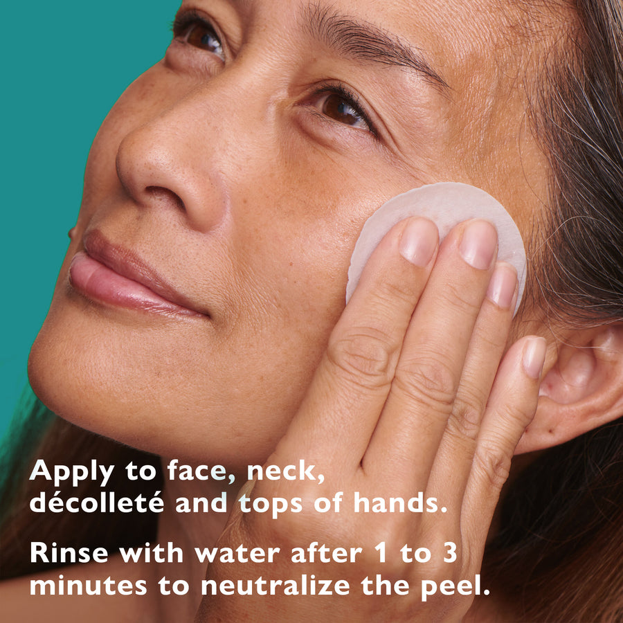 Person applying a round white exfoliating pad to cheek against turquoise background.