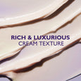 Swatches of pale cream and beige eye cream with glossy, smooth texture on purple-tinted background.