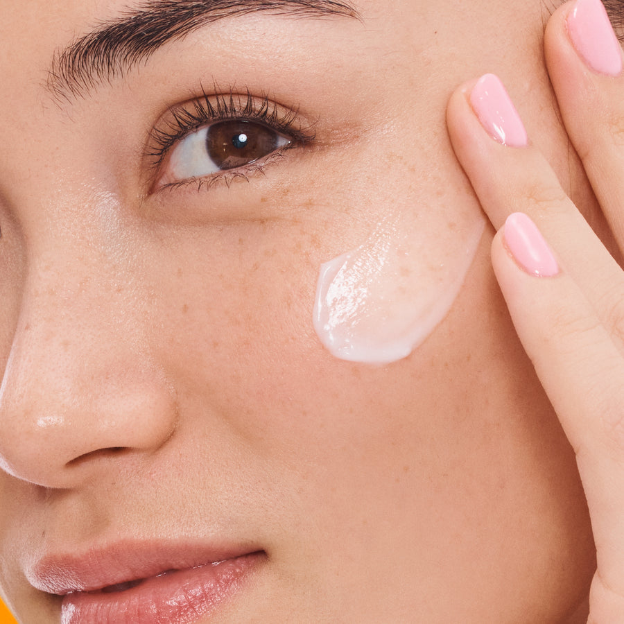 Clear gel serum applied to cheek of person with fair skin and pink nail polish.