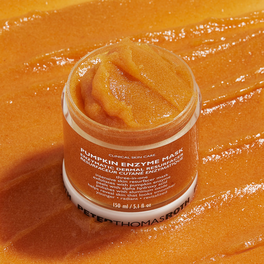 Orange pumpkin enzyme mask in white jar with textured surface displayed against pumpkin-colored background.