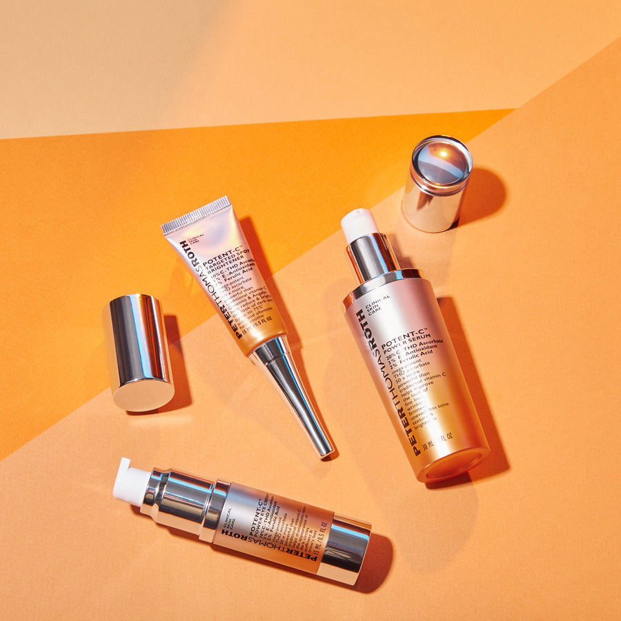 White tube and rose-gold applicator of Potent-C Power Eye Cream displayed with matching skincare products on orange backgroun